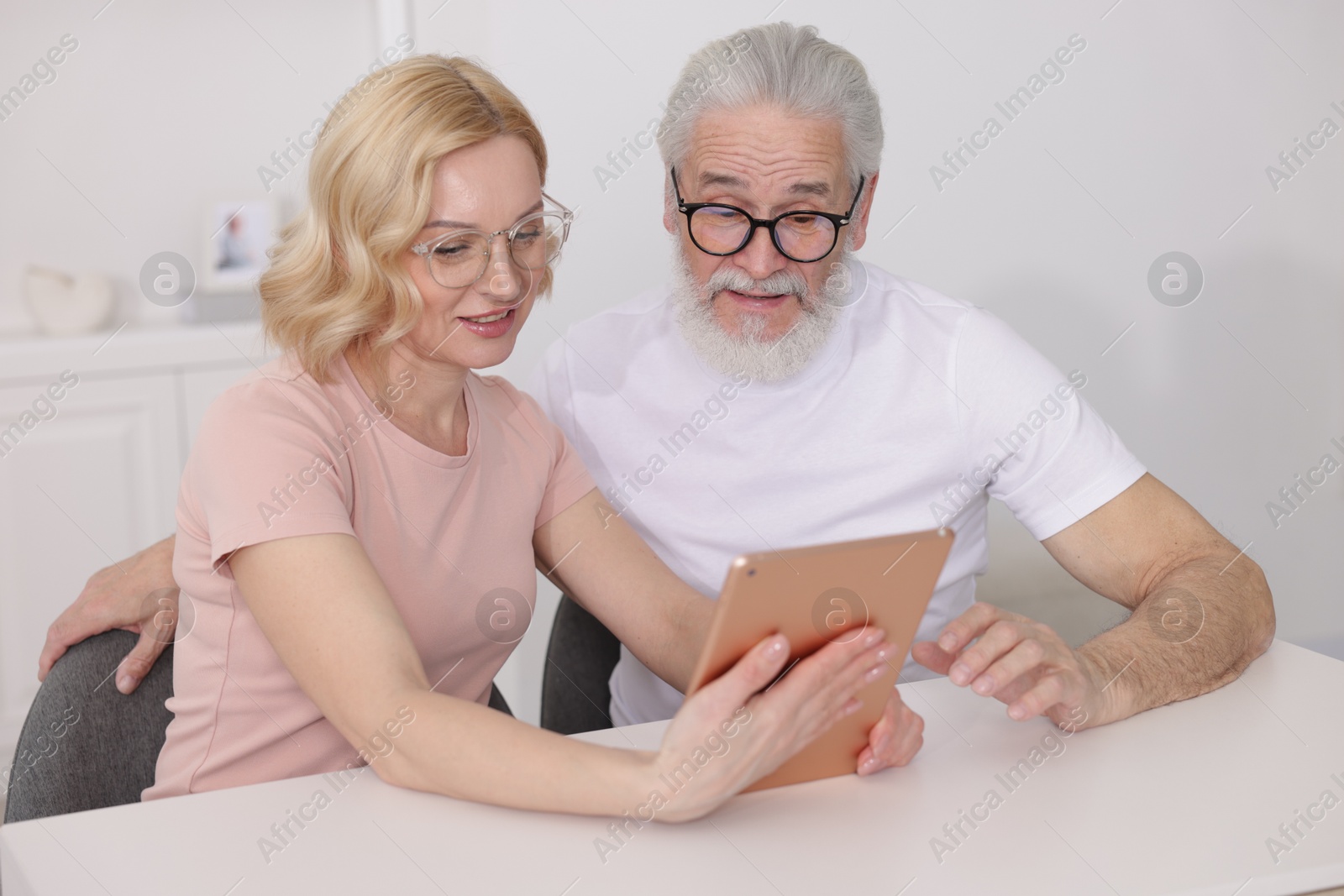 Photo of Senior man and mature woman watching something on tablet at home. Happy couple