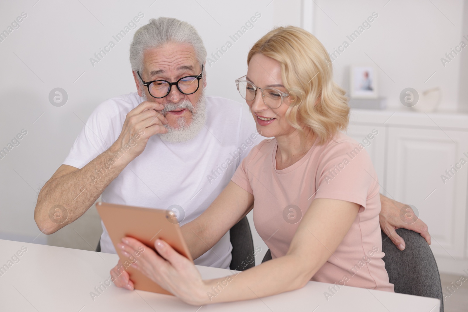 Photo of Senior man and mature woman watching something on tablet at home. Happy couple