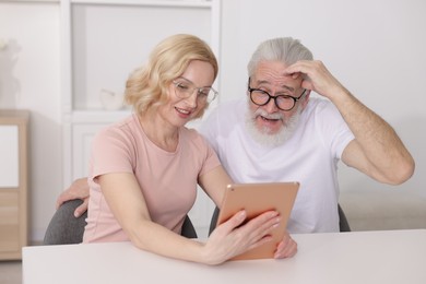 Photo of Senior man and mature woman watching something on tablet at home. Happy couple