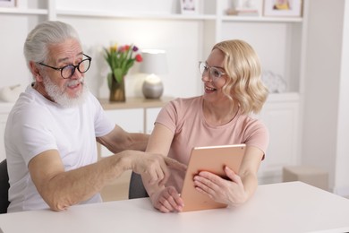 Photo of Senior man and mature woman with tablet spending time together at home. Happy couple