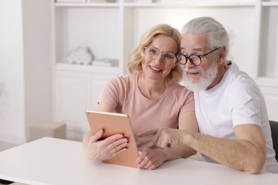 Photo of Senior man and mature woman watching something on tablet at home. Happy couple