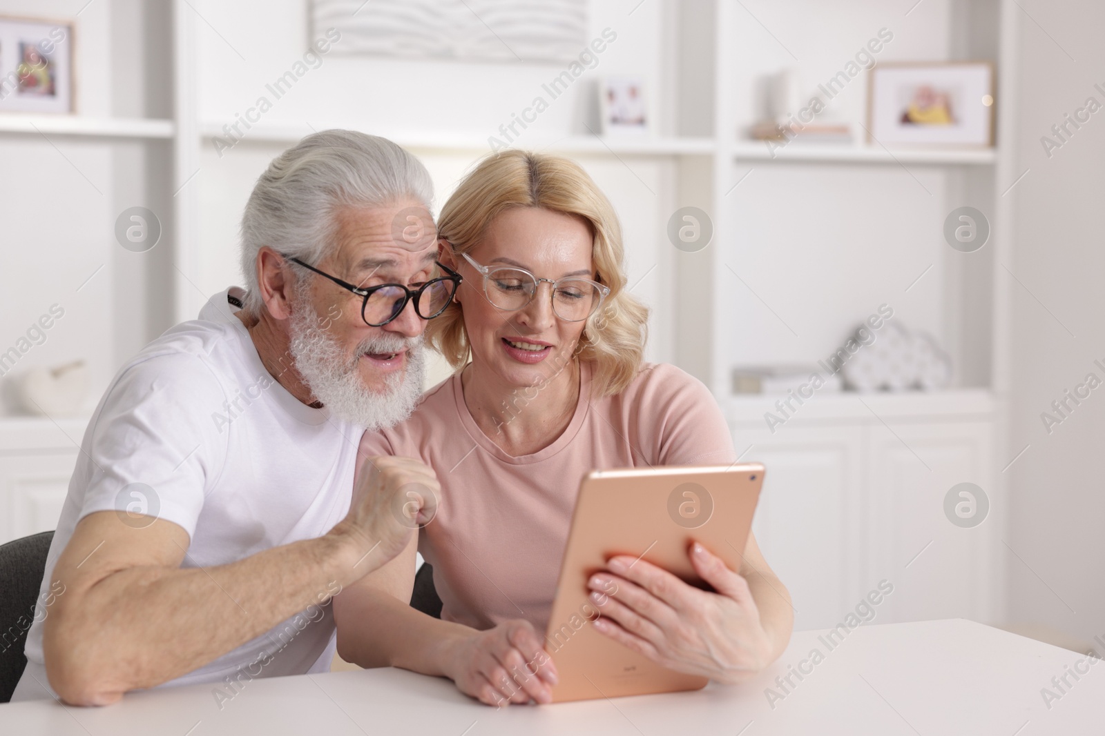 Photo of Senior man and mature woman watching something on tablet at home. Happy couple