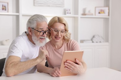 Senior man and mature woman watching something on tablet at home. Happy couple