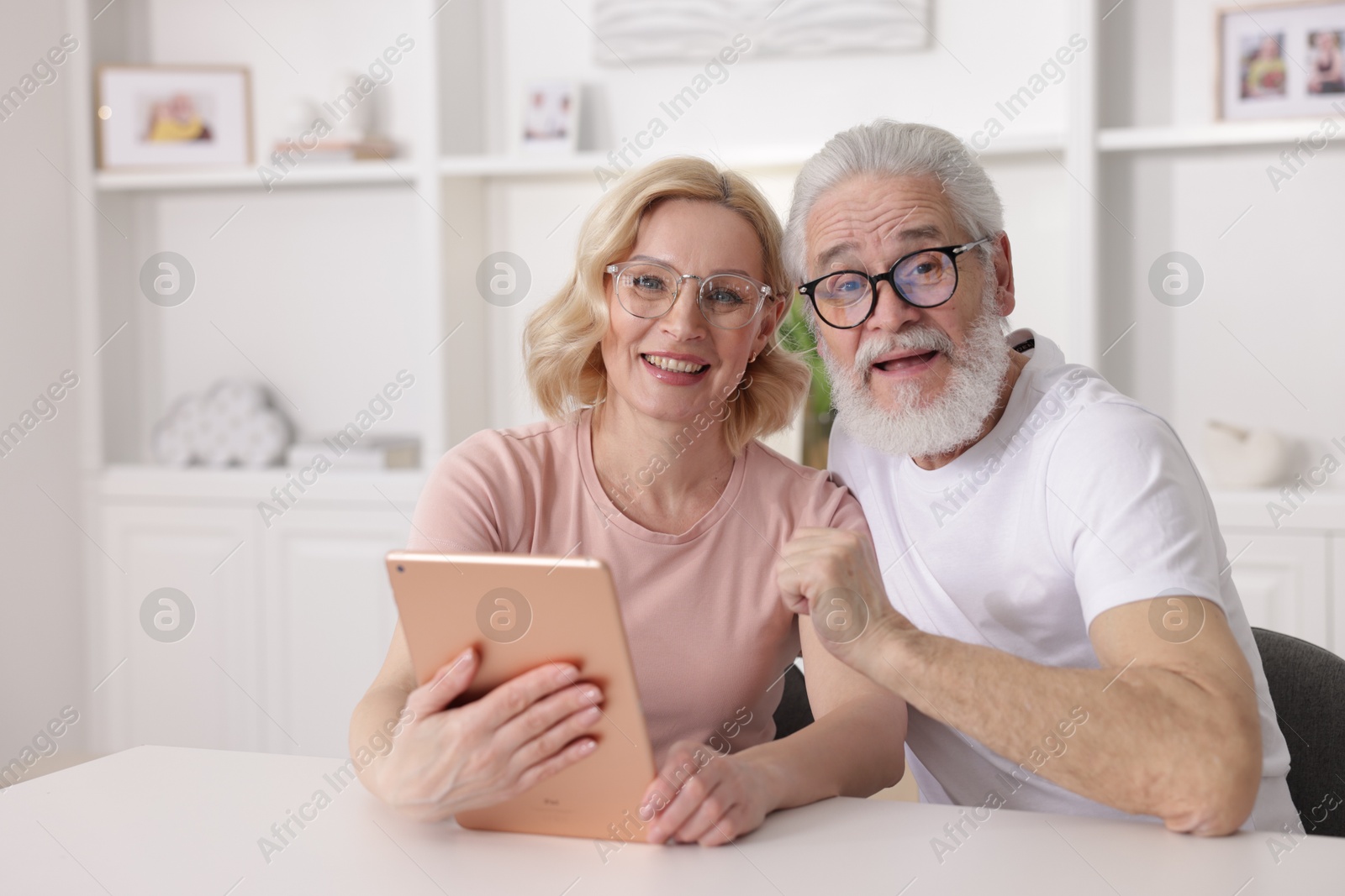 Photo of Senior man and mature woman with tablet spending time together at home. Happy couple