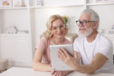 Senior man and mature woman watching something on tablet at home. Happy couple