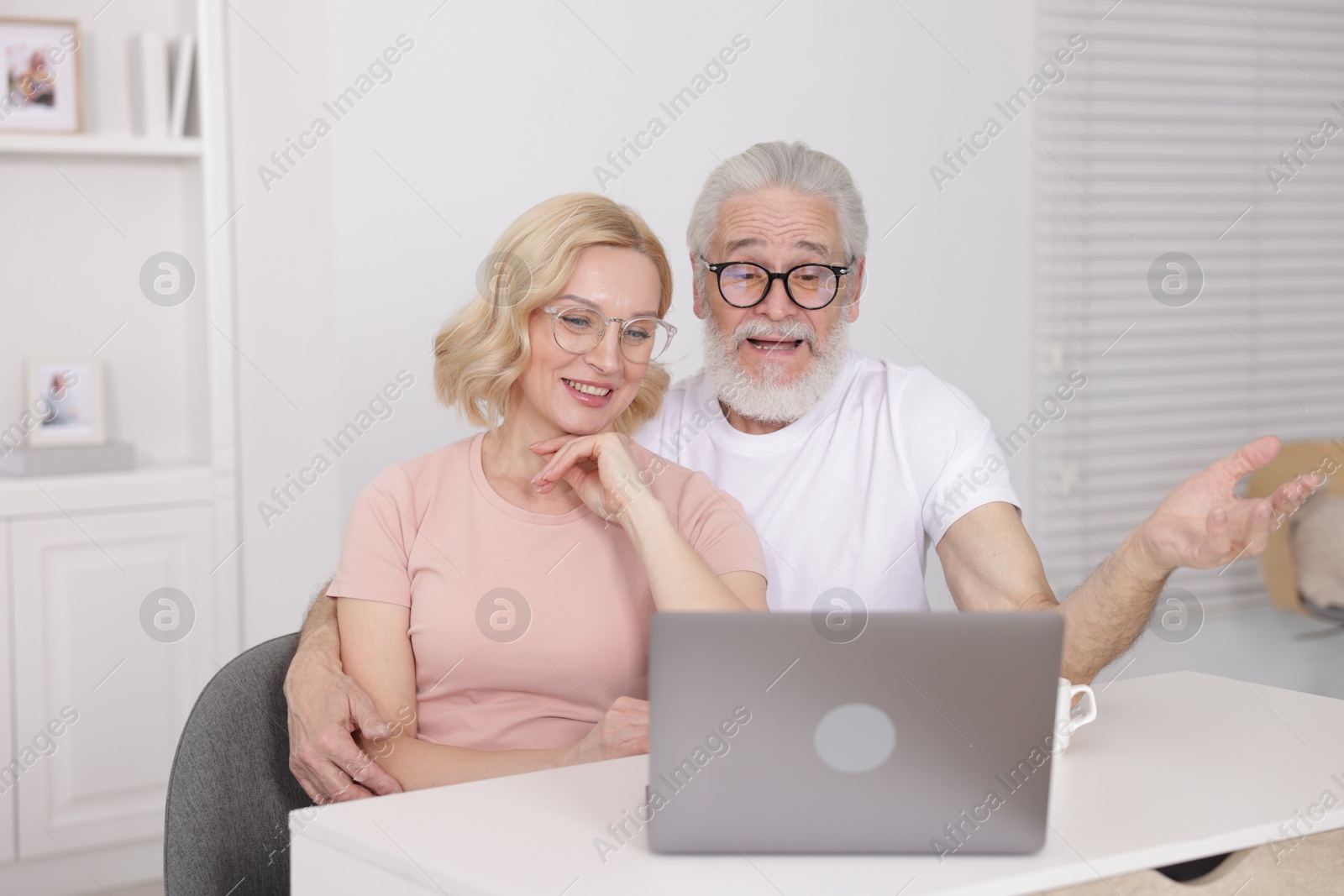 Photo of Senior man and mature woman watching something on laptop at home. Happy couple