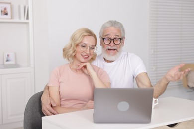 Photo of Senior man and mature woman watching something on laptop at home. Happy couple