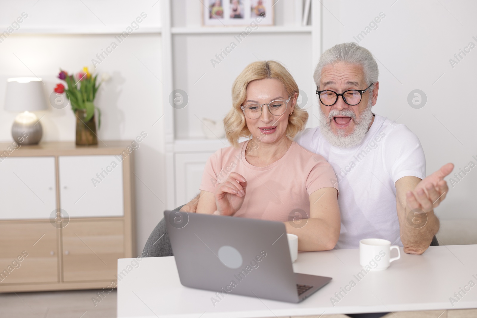 Photo of Senior man and mature woman watching something on laptop at home. Happy couple