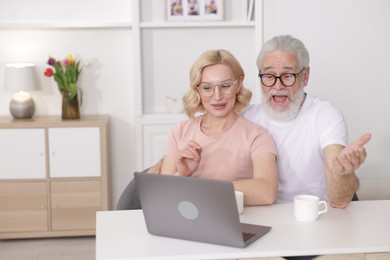 Senior man and mature woman watching something on laptop at home. Happy couple