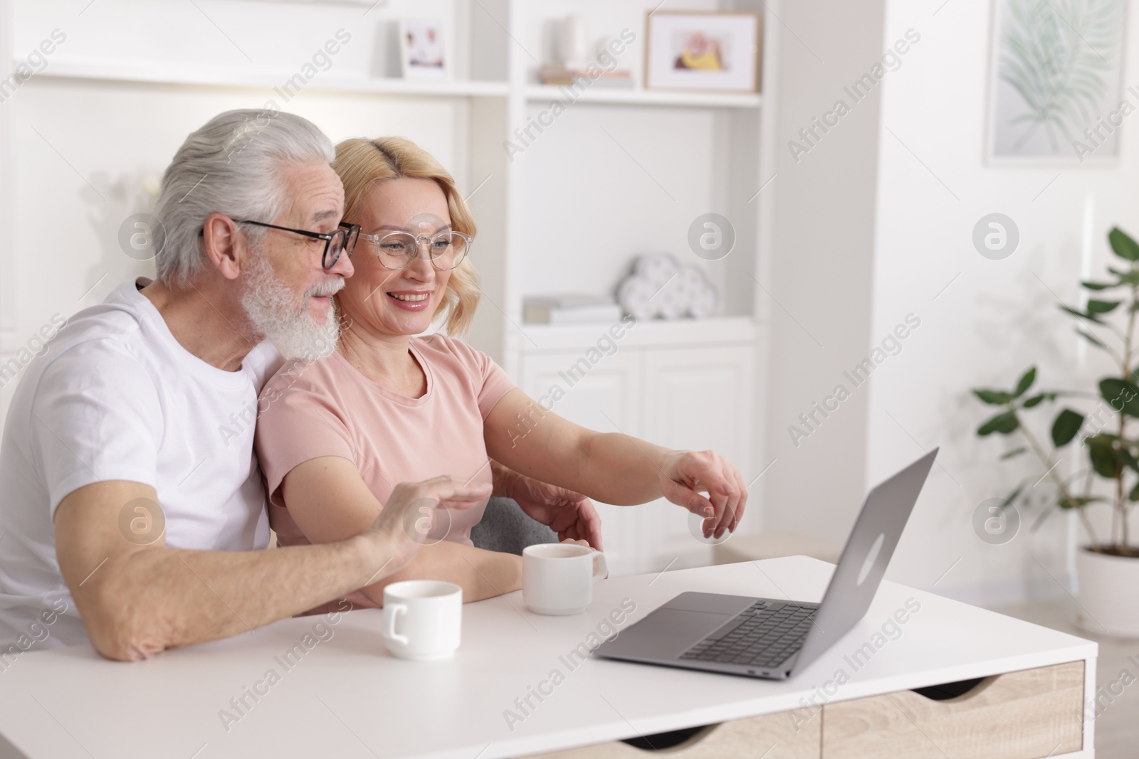 Photo of Senior man and mature woman watching something on laptop at home. Happy couple