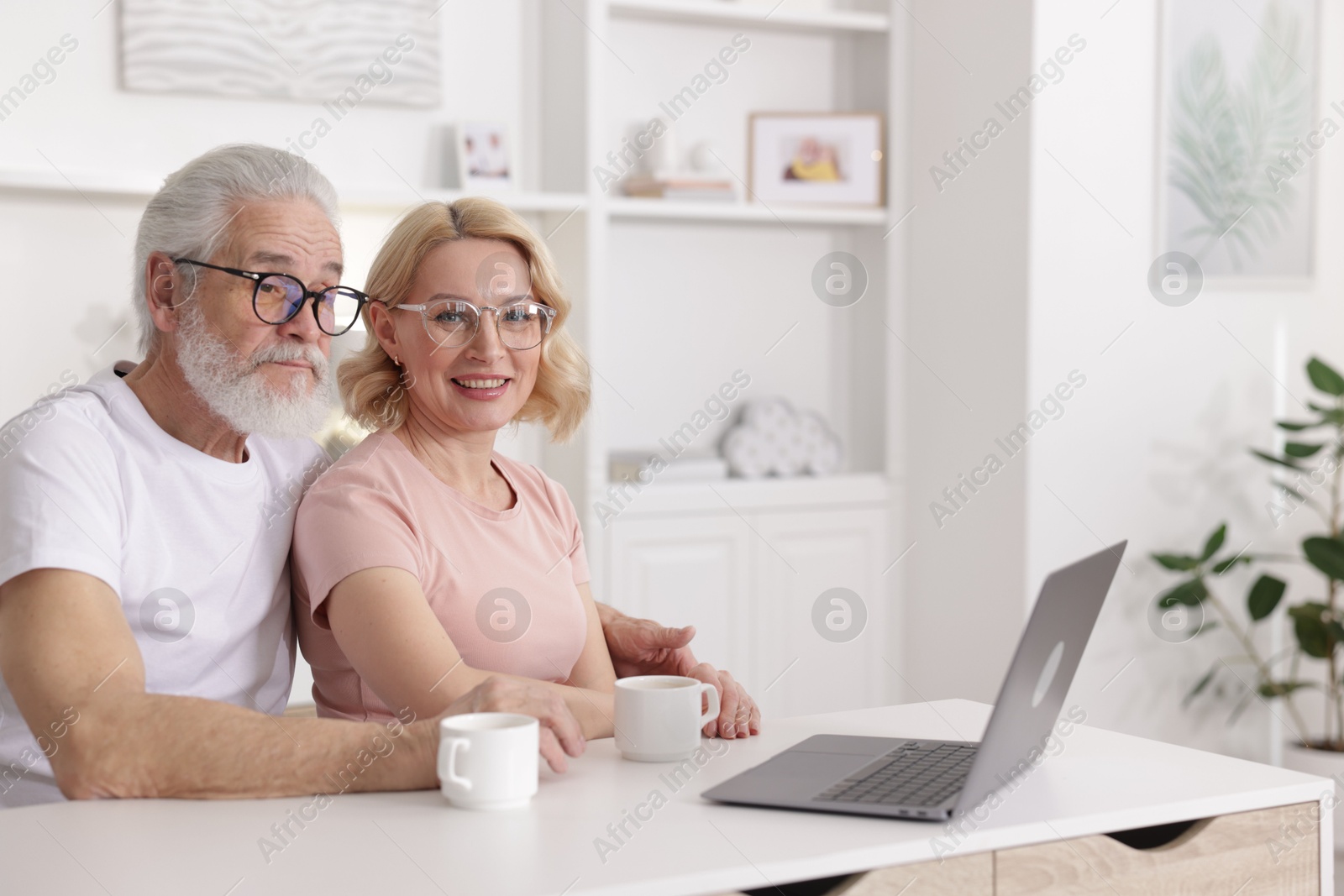 Photo of Senior man and mature woman with laptop spending time together at home. Happy couple