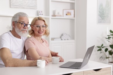 Senior man and mature woman with laptop spending time together at home. Happy couple