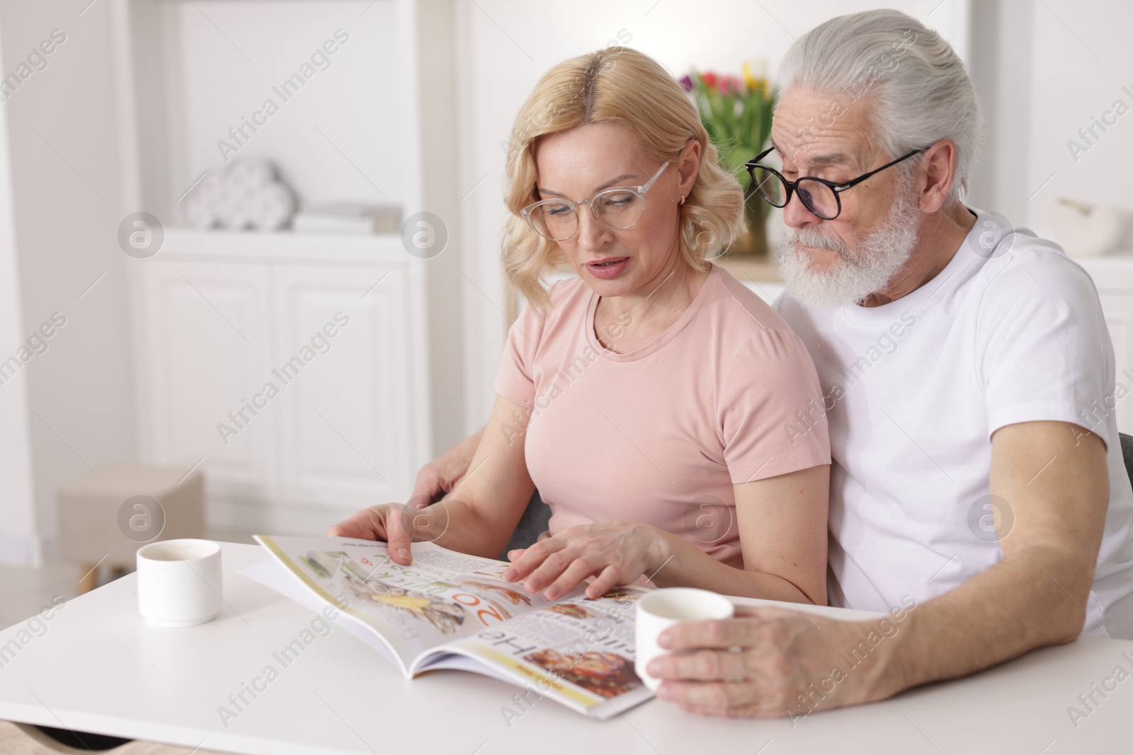 Photo of Senior man and mature woman reading magazine at home. Happy couple