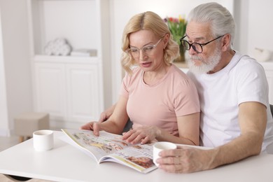 Photo of Senior man and mature woman reading magazine at home. Happy couple