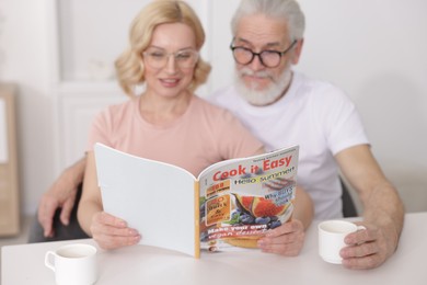 Senior man and mature woman reading magazine at home, selective focus. Happy couple