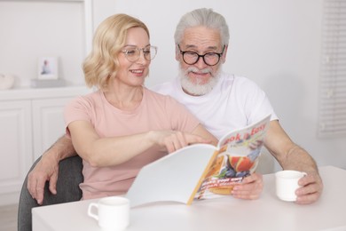 Senior man and mature woman reading magazine at home. Happy couple