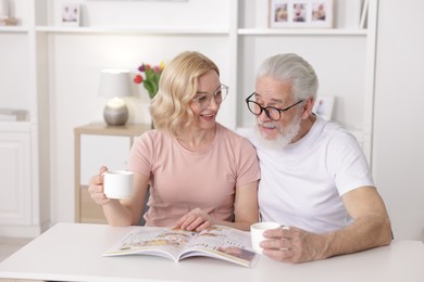 Photo of Senior man and mature woman with coffee reading magazine at home. Happy couple