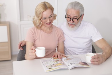 Senior man and mature woman with coffee reading magazine at home. Happy couple