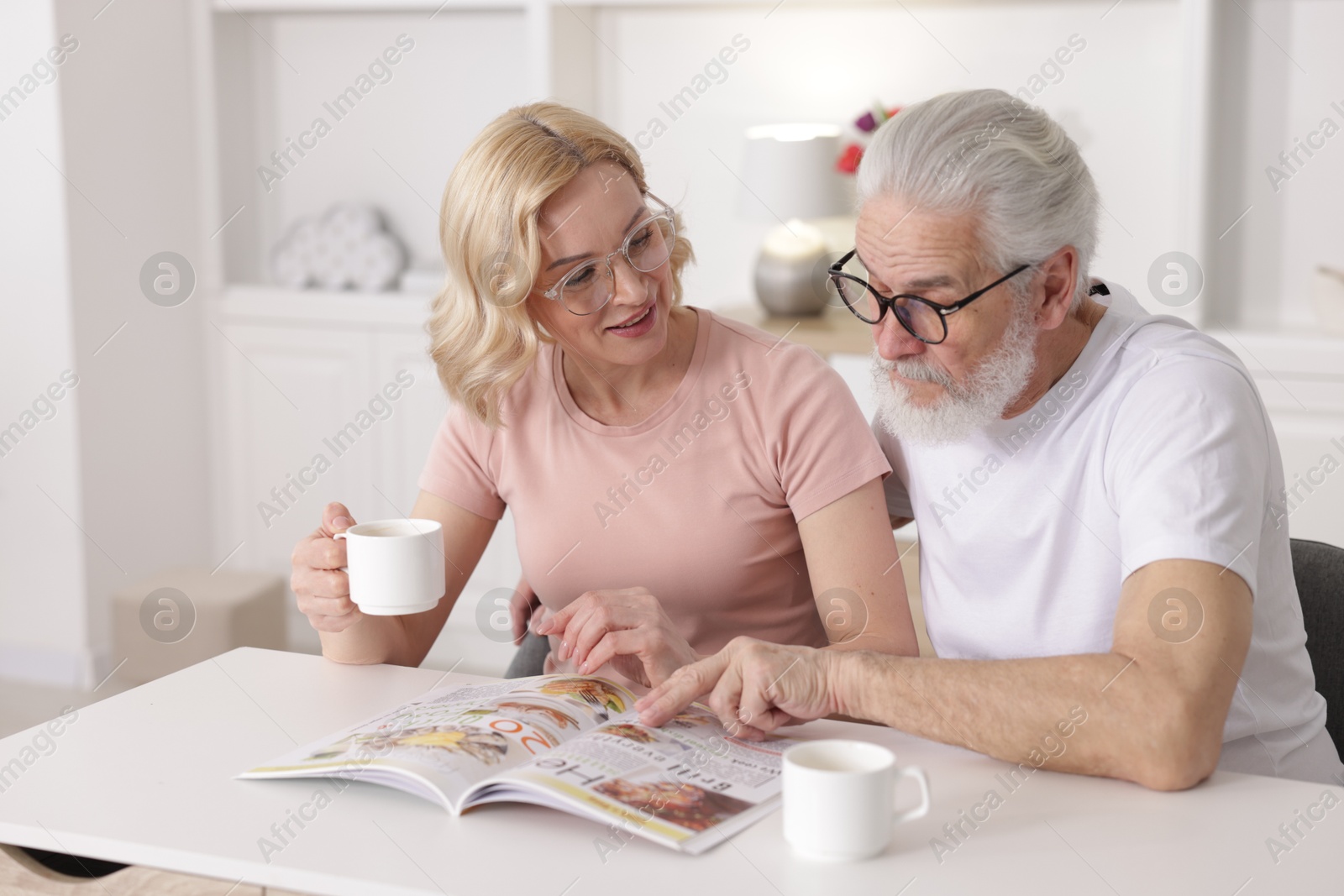 Photo of Senior man and mature woman with coffee reading magazine at home. Happy couple