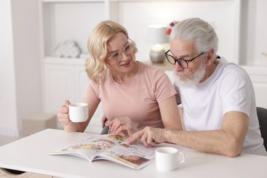 Photo of Senior man and mature woman with coffee reading magazine at home. Happy couple