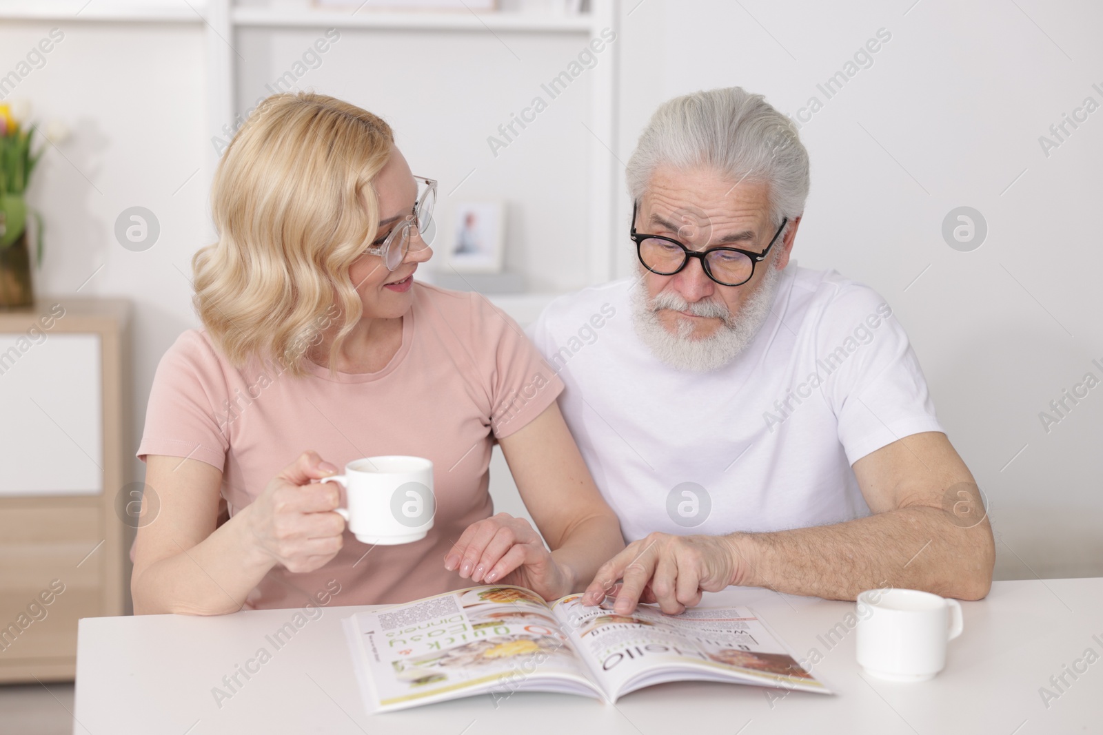 Photo of Senior man and mature woman with coffee reading magazine at home. Happy couple