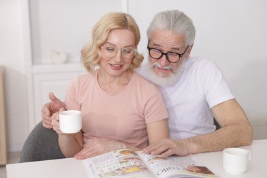 Photo of Senior man and mature woman with coffee reading magazine at home. Happy couple