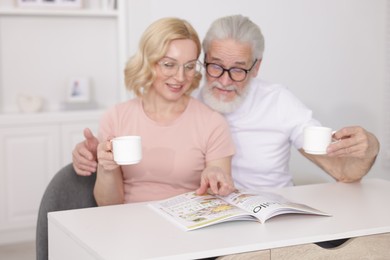 Photo of Senior man and mature woman with coffee reading magazine at home. Happy couple