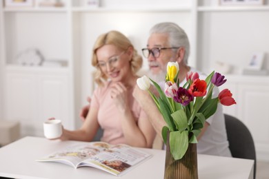 Photo of Senior man and mature woman spending time together at home, focus on tulips. Happy couple