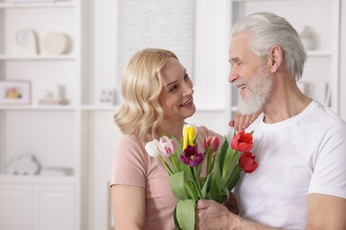 Photo of Senior man with colorful tulips and mature woman at home. Happy couple