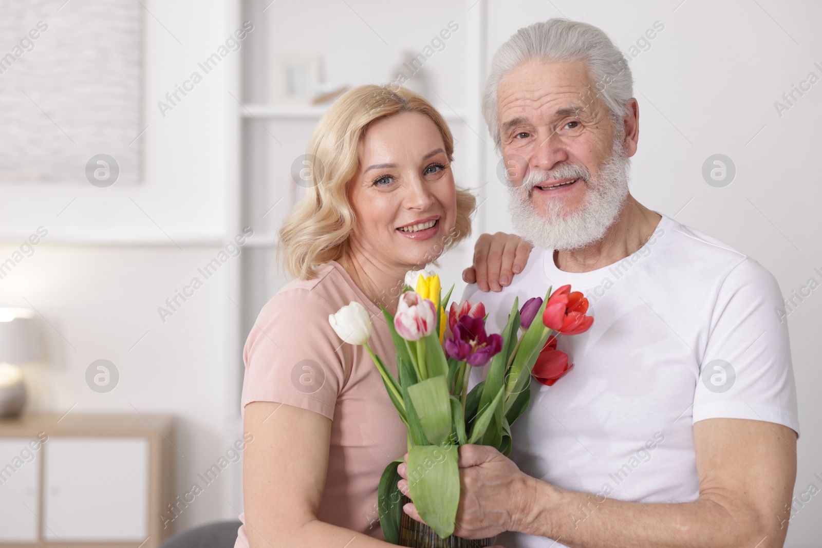 Photo of Senior man with colorful tulips and mature woman at home. Happy couple