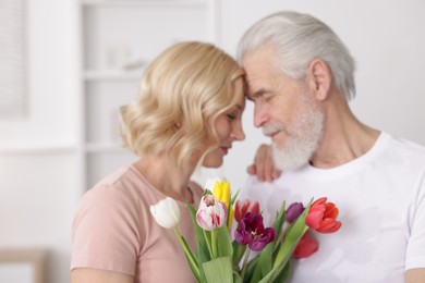 Senior man and mature woman with colorful tulips at home. Happy couple