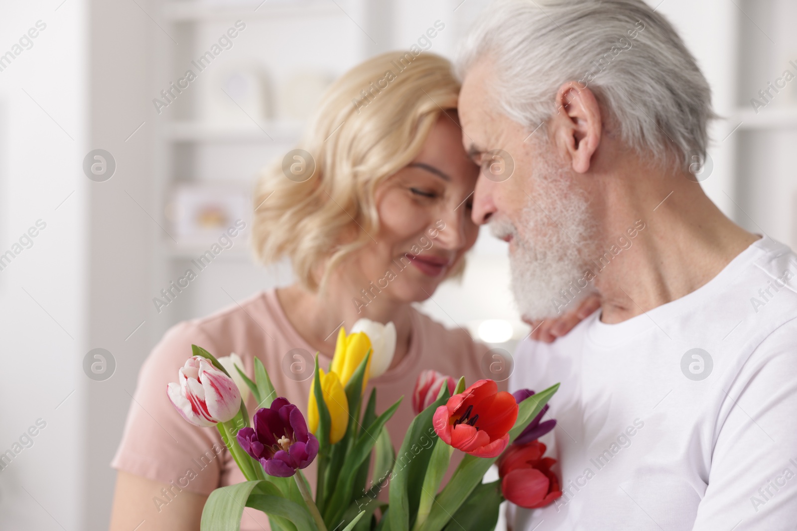 Photo of Senior man and mature woman with colorful tulips at home. Happy couple