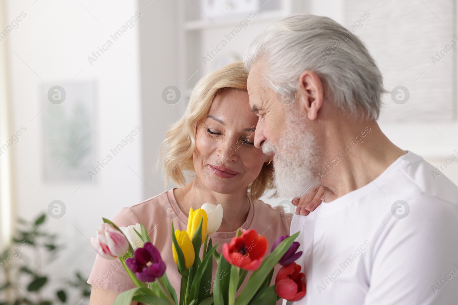 Photo of Senior man and mature woman with colorful tulips at home. Happy couple