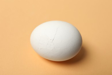 Photo of One egg with cracked shell on beige background, closeup