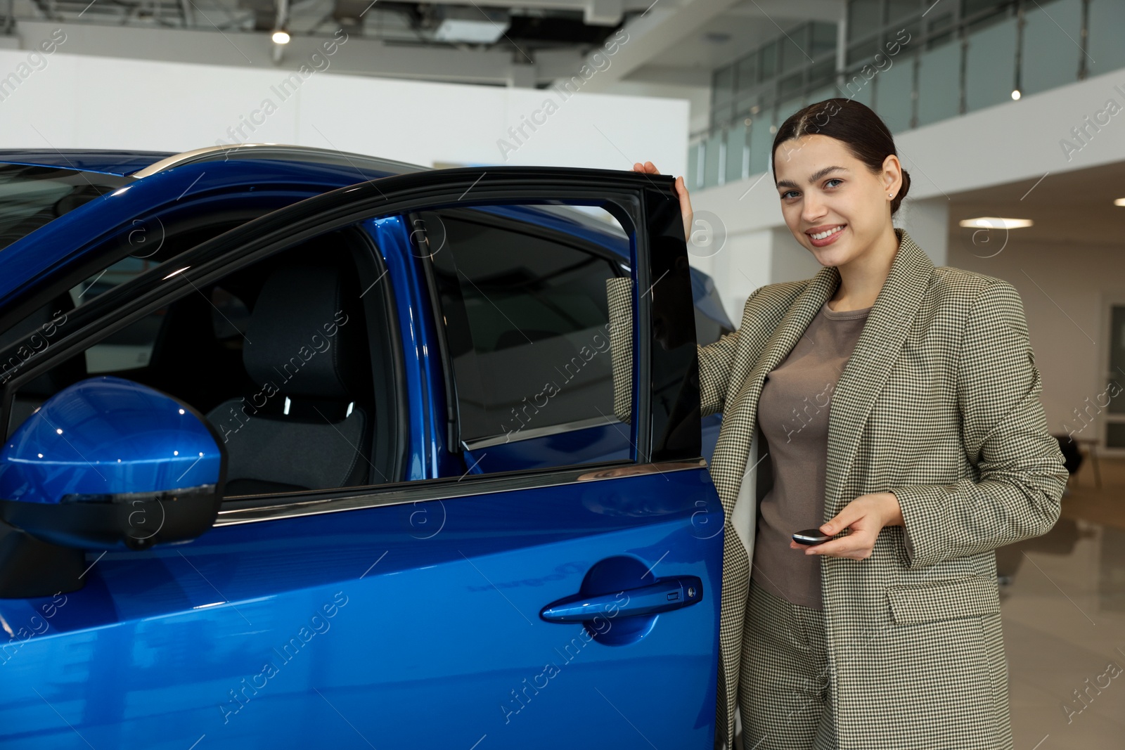 Photo of Happy saleswoman near new blue car in salon