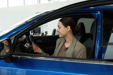 Happy woman with key inside new car in salon