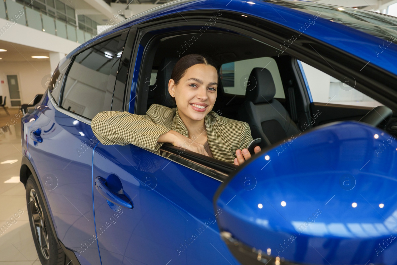 Photo of Happy woman with key inside new car in salon