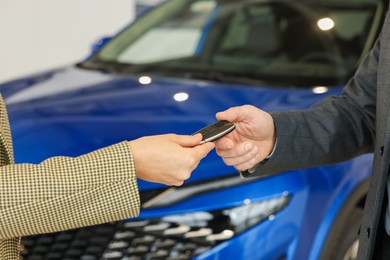 Saleswoman giving car key to client in salon, closeup