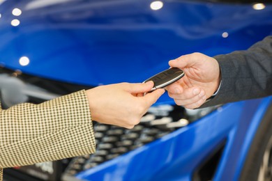 Photo of Saleswoman giving car key to client in salon, closeup