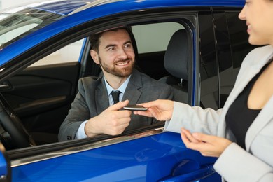 Happy saleswoman giving key to client inside new car in salon