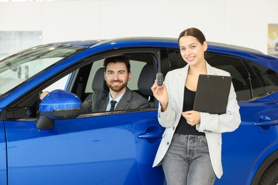 Happy saleswoman with key and client inside new car in salon