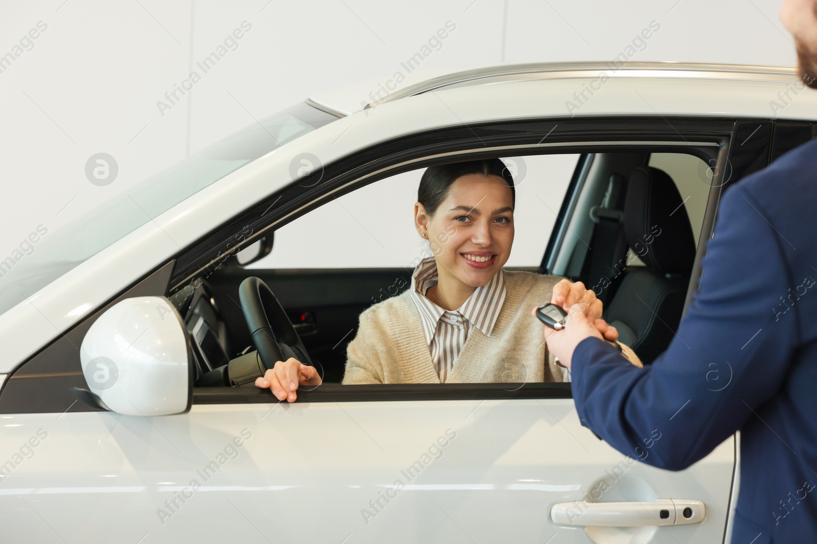 Photo of Salesman giving key to happy client inside new car in salon