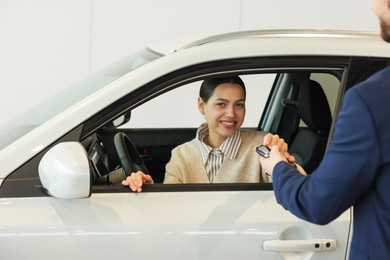 Photo of Salesman giving key to happy client inside new car in salon