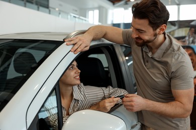 Happy husband giving key to his wife inside new car in salon