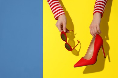 Photo of Woman showing red high-heeled shoe and sunglasses on color background, closeup with space for text. Stylish presentation