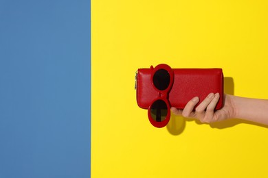 Photo of Woman showing red wallet and sunglasses on color background, closeup with space for text. Stylish presentation