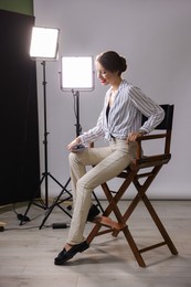 Beautiful woman with script sitting in director's chair in studio