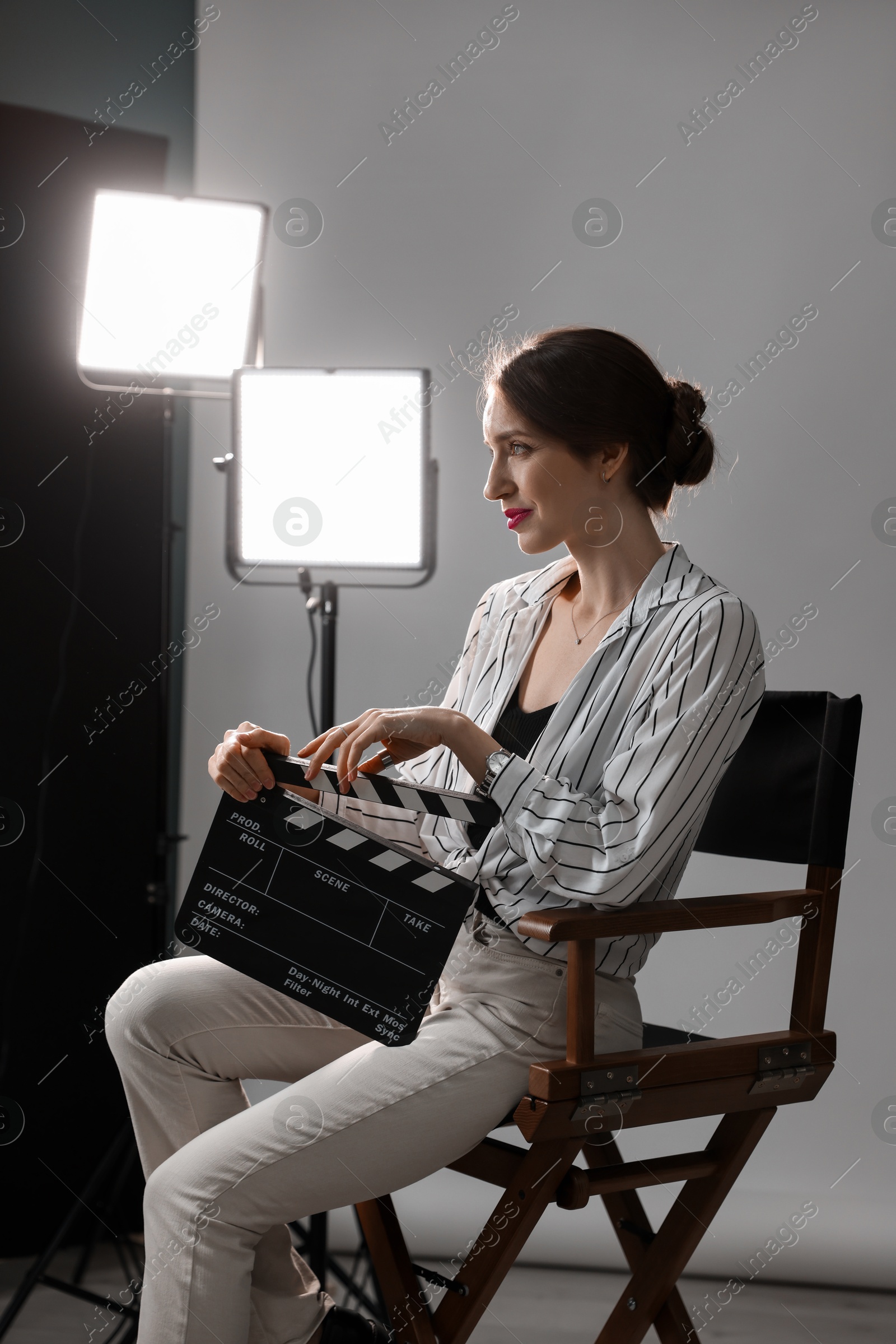 Photo of Beautiful woman with clapperboard sitting in director's chair in studio