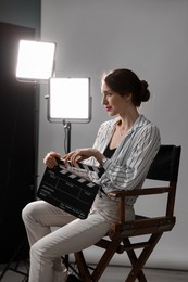 Beautiful woman with clapperboard sitting in director's chair in studio