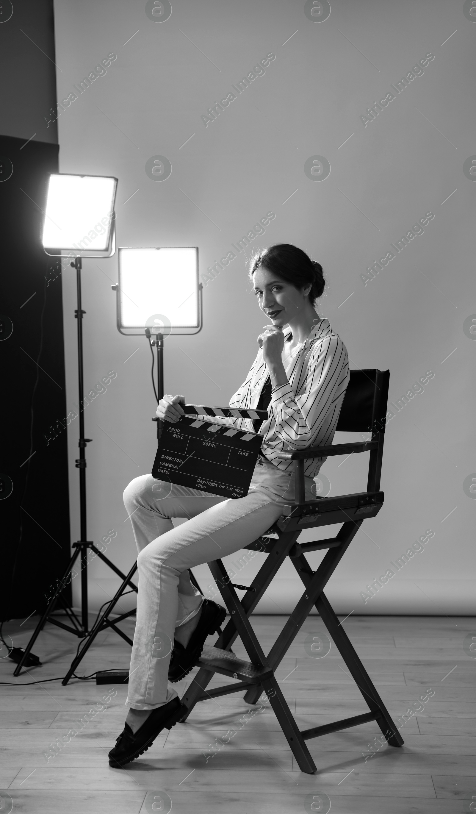 Photo of Beautiful woman with clapperboard sitting in director's chair in studio. Black and white effect